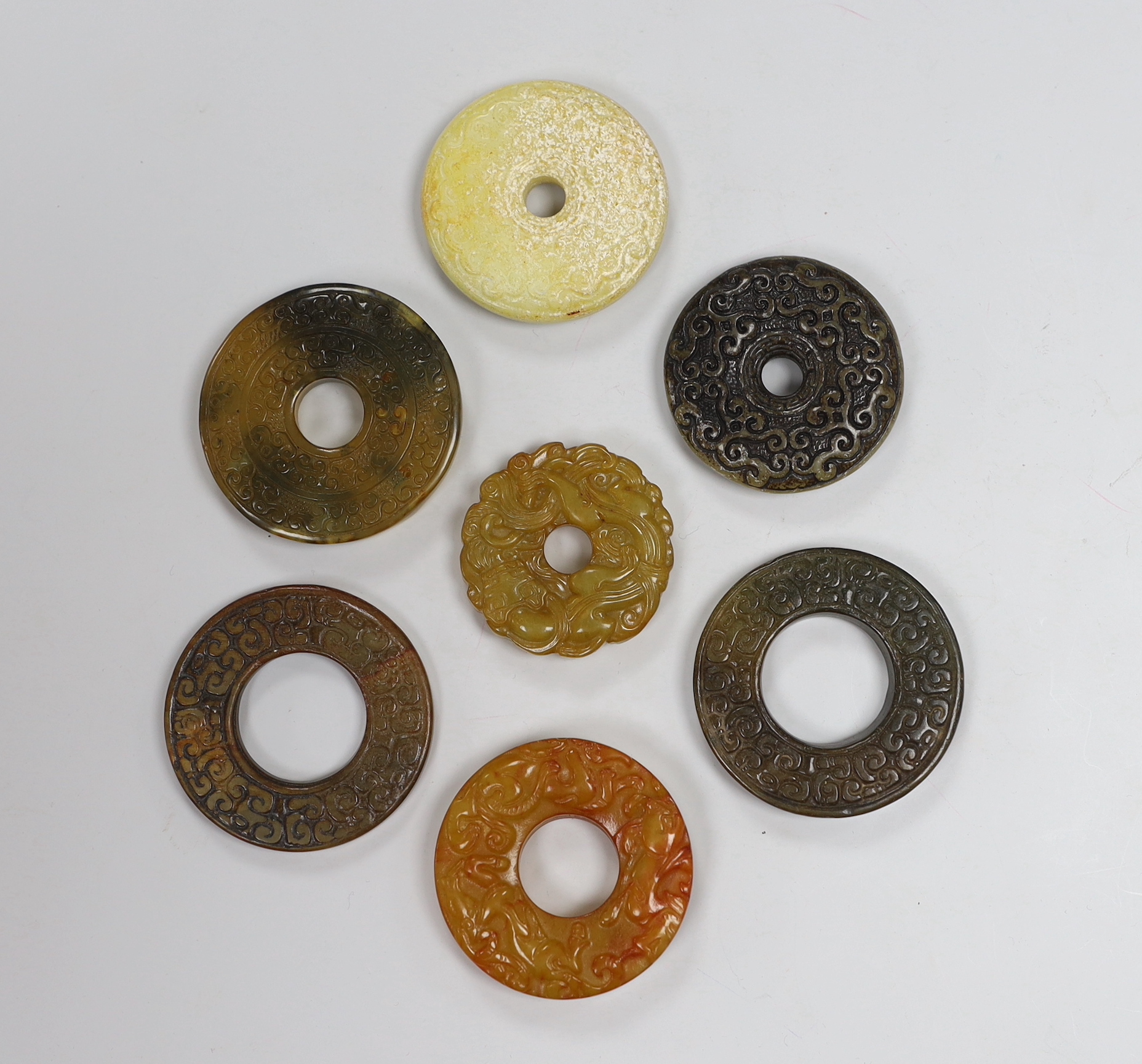 Seven Chinese jade or hardstone bi discs with carved decoration, the largest 5cm in diameter